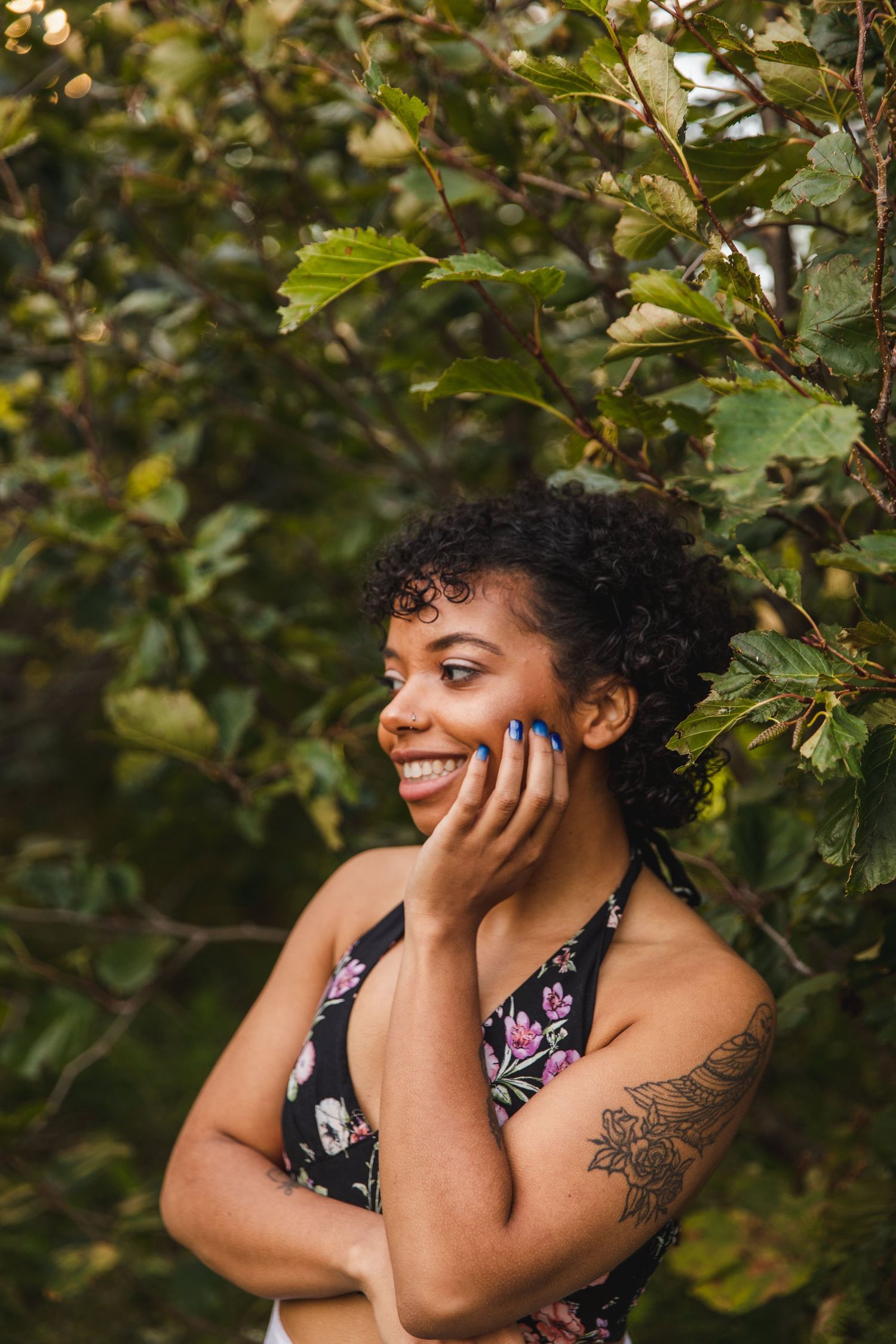 Portrait of someone smiling with hand on face against green foliage background.