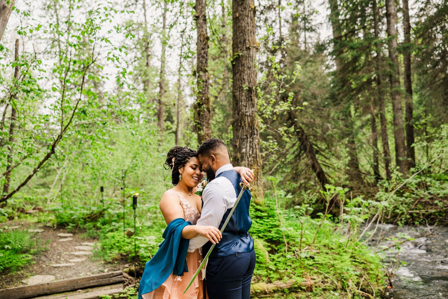 A couple embraces on a forest path surrounded by lush green vegetation.