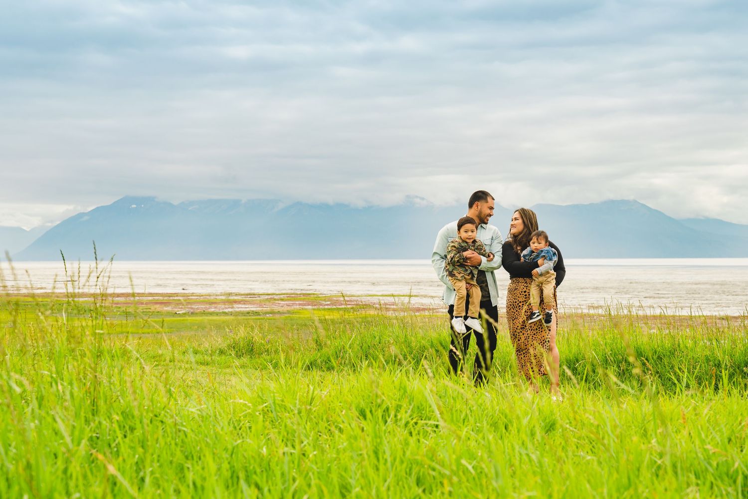 Family silhouetted against mountain vista in tall grass meadow at sunset.