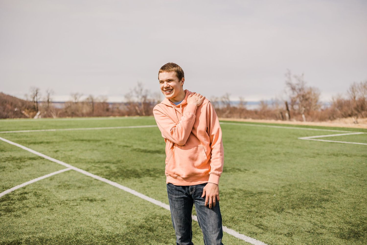 Person in peach hoodie standing on soccer field lines during cloudy day.