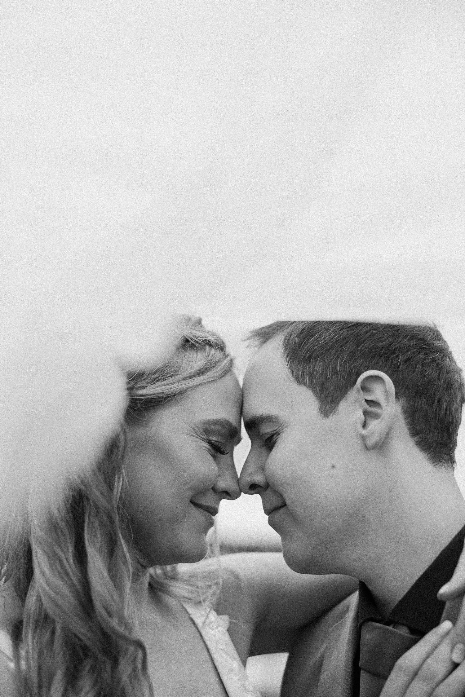 A romantic black and white portrait of a couple touching foreheads intimately while smiling.