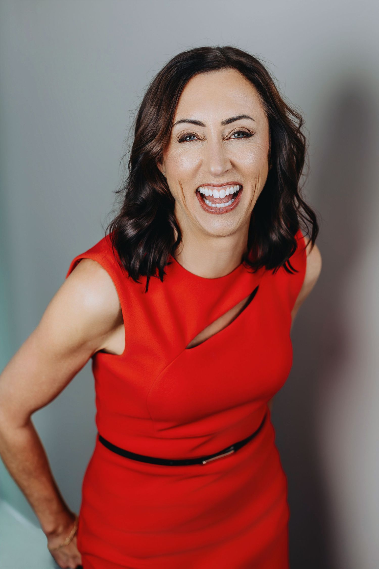 Woman in vibrant red dress smiling against grey background.