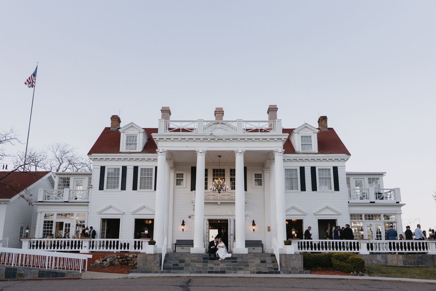 A couple photographed outside their wedding venue with guest in the background.