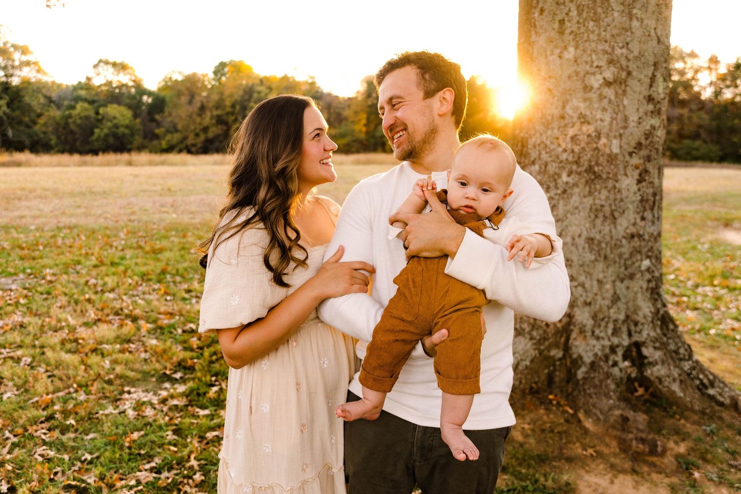 Family of three shares intimate moment together under tree during golden hour.