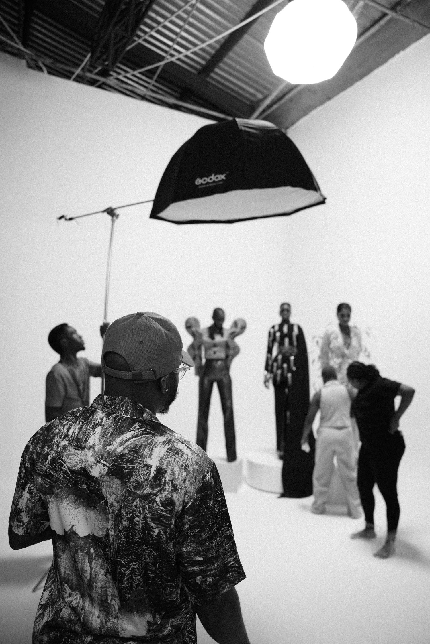 Black and white photo of photo studio setup showing lighting equipment and subjects in background.