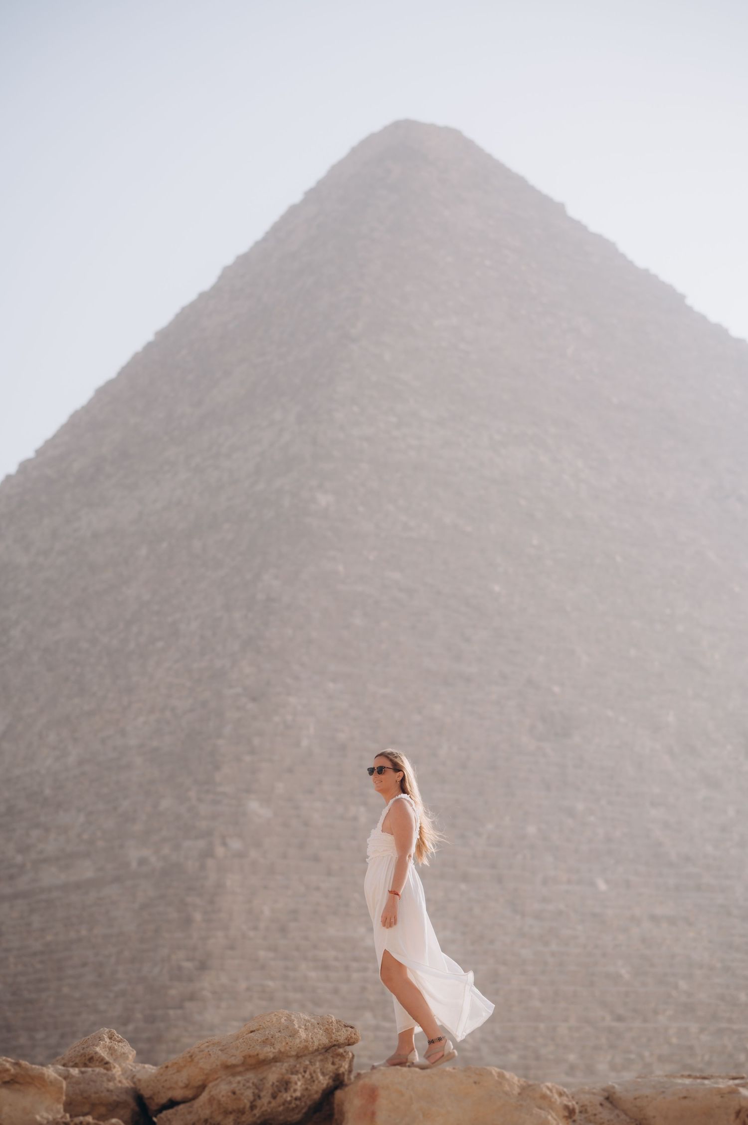White-dressed figure stands on rocky outcrop before massive pyramid in Egypt.
