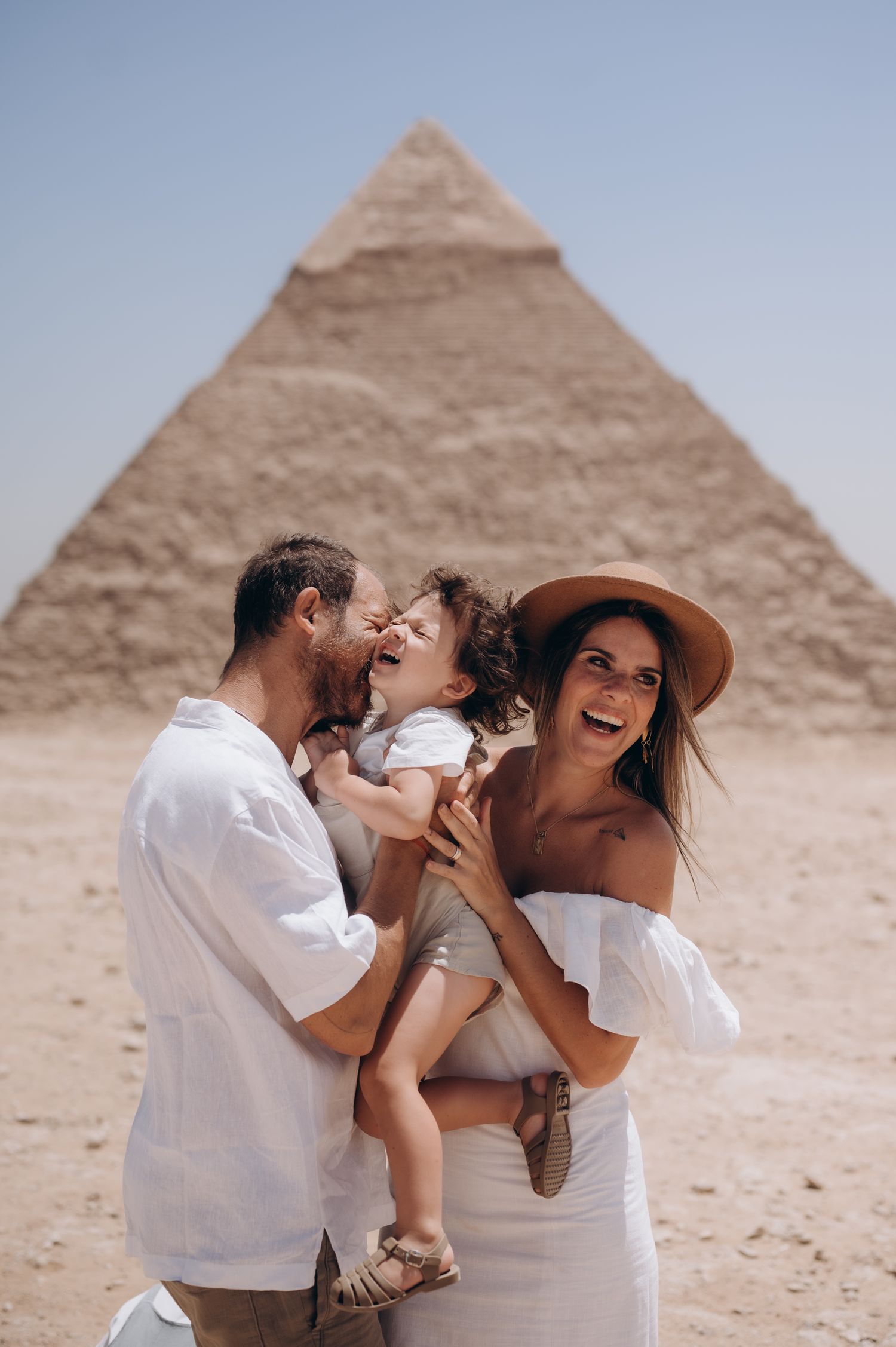 Family shares joyful moment together in white outfits before Egyptian pyramid.