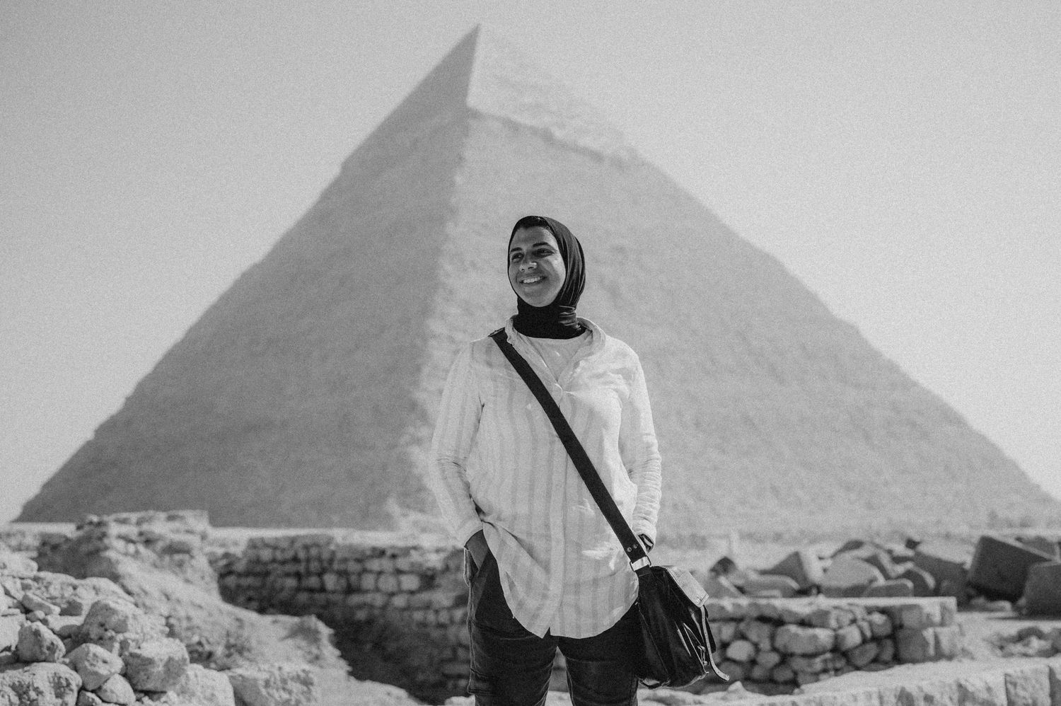 A figure in traditional Egyptian dress stands among ancient pyramids in a black and white historical photograph.
