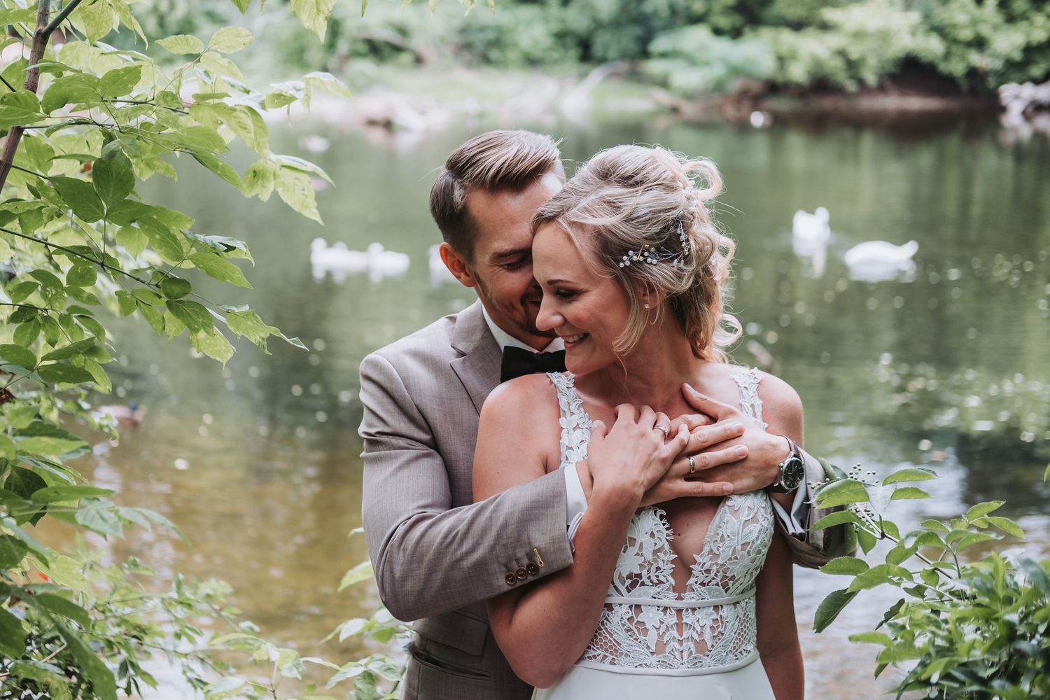 Romantic wedding photo shoot by a pond with swans in natural setting.
