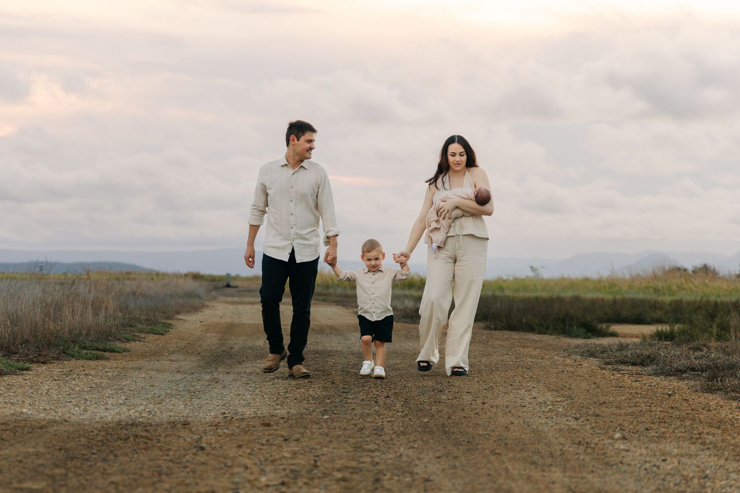 Family wearing white outfits walks together on a hilltop path during golden hour.