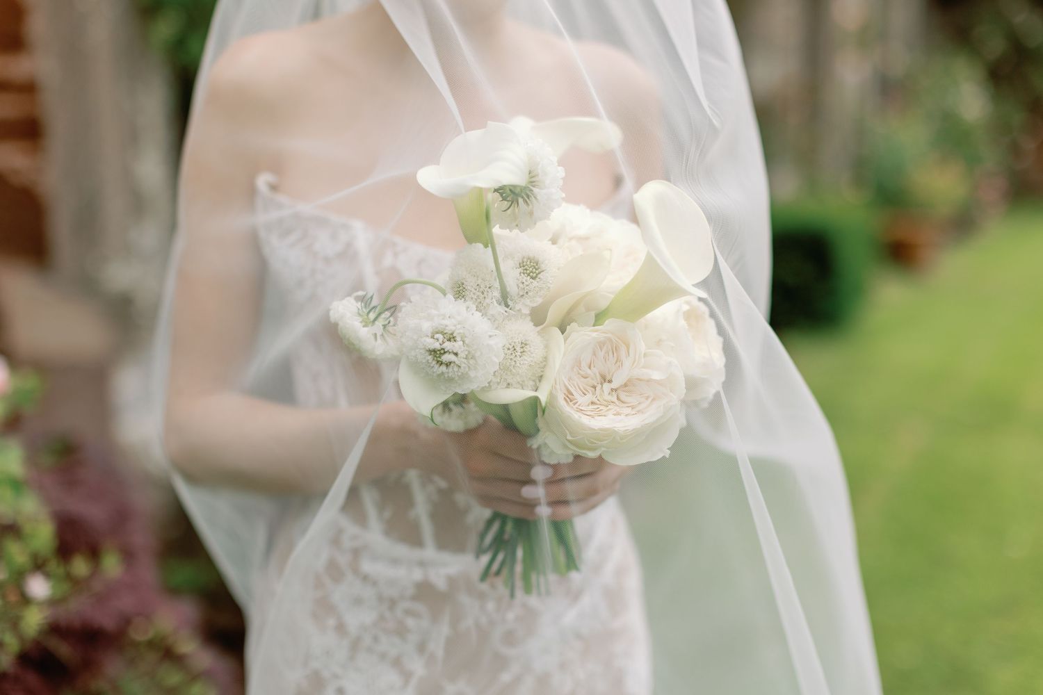 Delicate white rose bouquet held by someone in a lace wedding dress with veil.