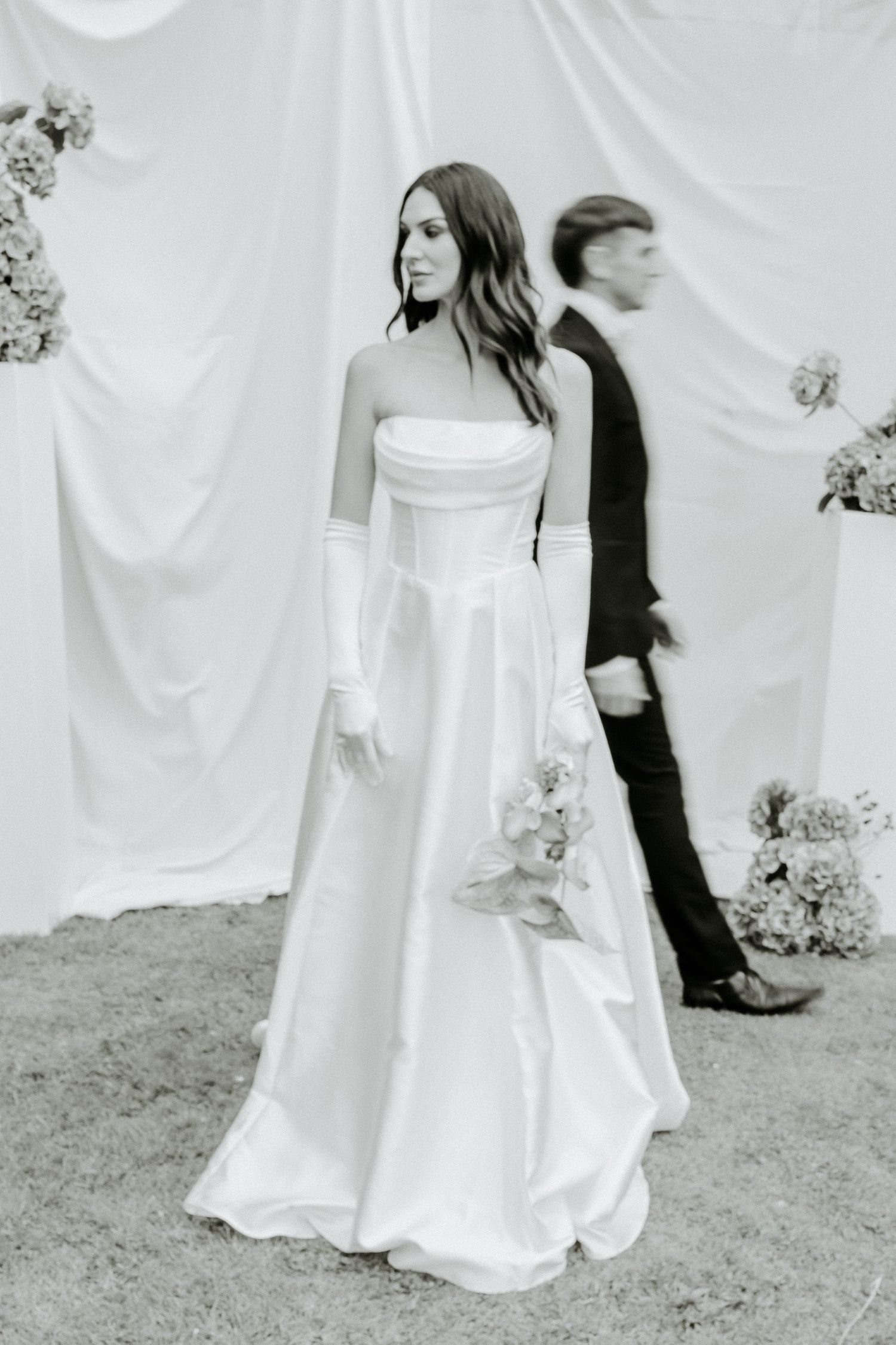 Elegant wedding scene in black and white with flowing white dress and dramatic fabric backdrop.