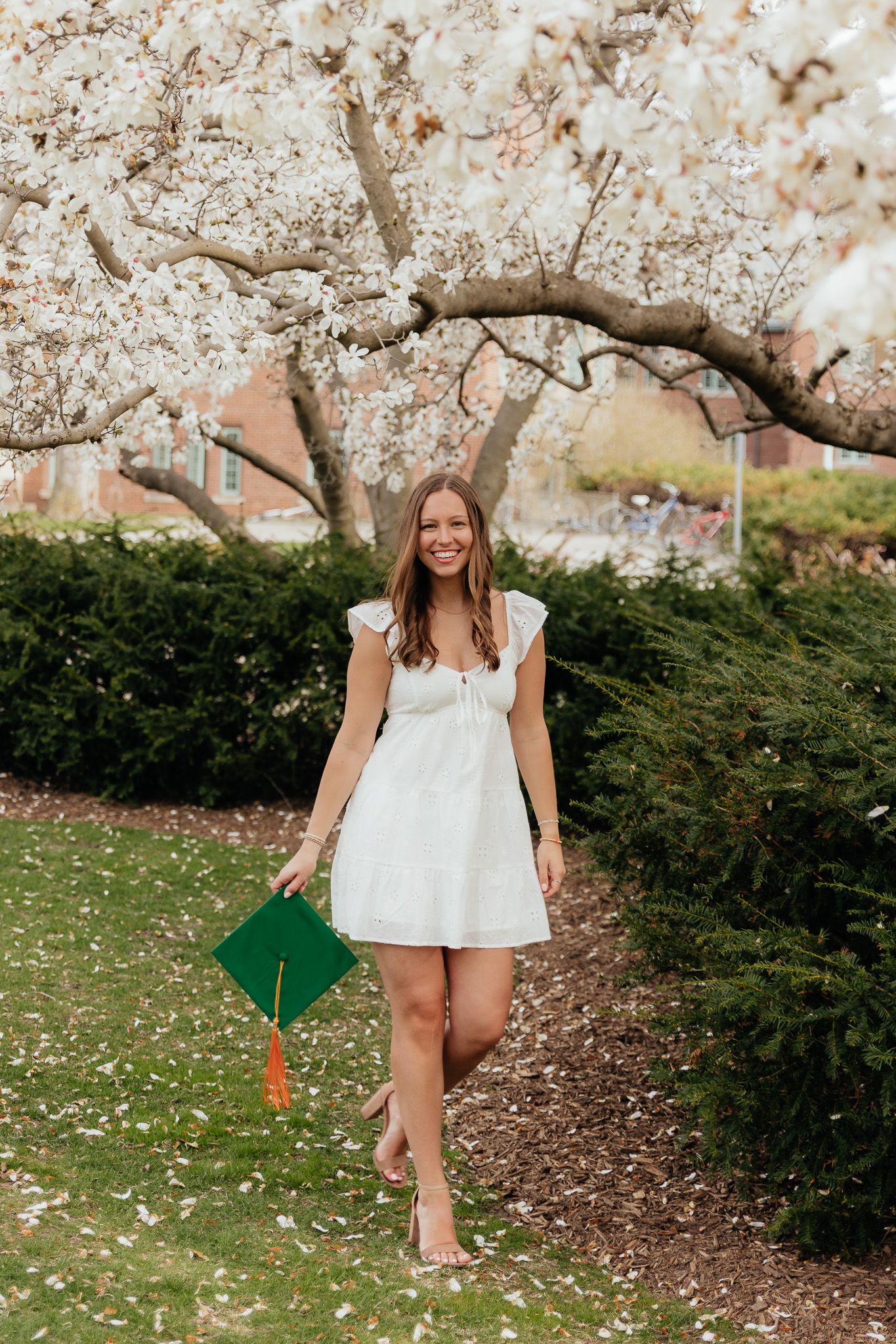 MSU graduate walking and smiling while holding her graduation cap in East Lansing, Michigan, photographed by Brena B Imagery.