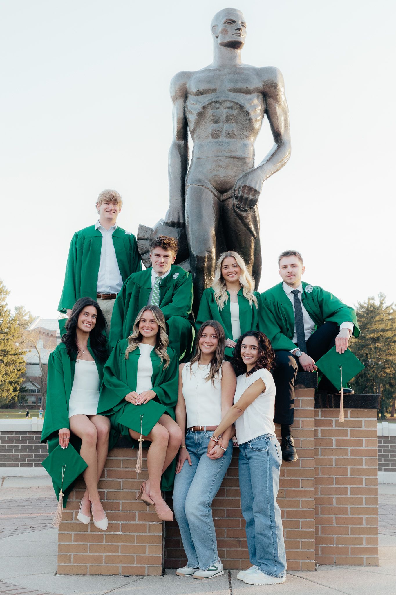 Friends celebrating graduation at the Spartan statue in East Lansing, photographed by Brena B Imagery.