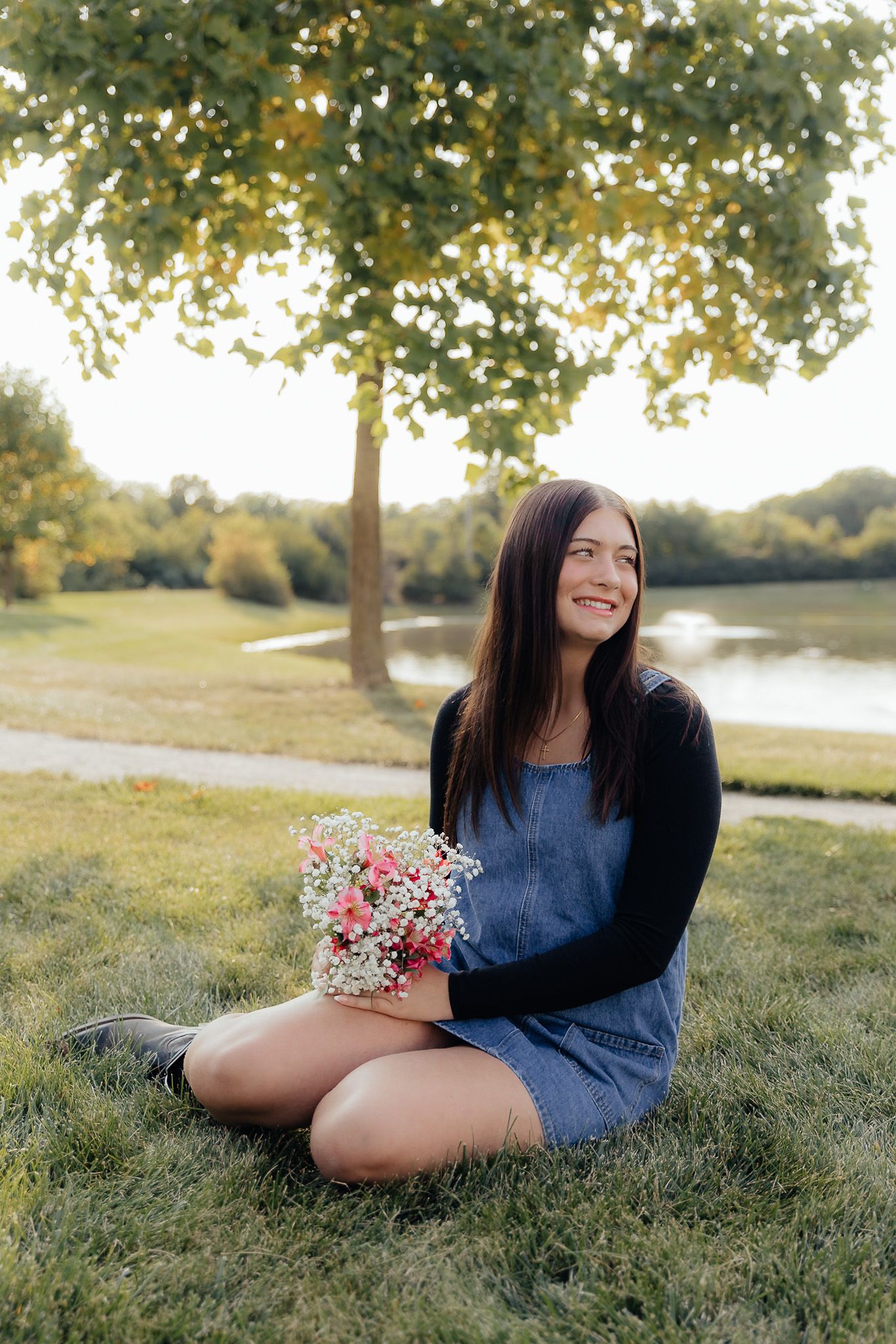 Dreamy golden hour senior session by Howell, Mi Senior Photographer Brena B Imagery. Senior Inspo girl sitting pose with bouquet at water