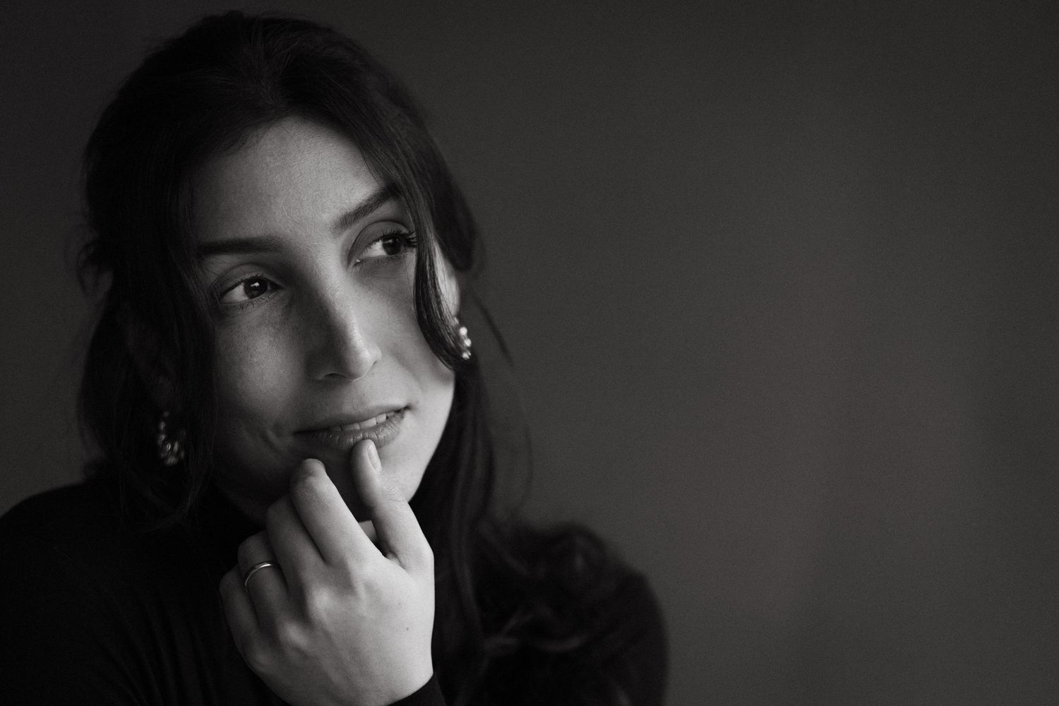 Intimate black and white portrait of a dark-haired woman smiling softly with hand near her face.