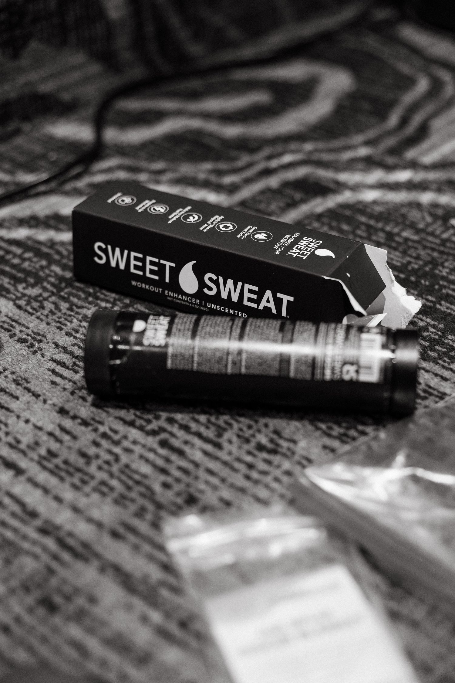 Black and white photo of Sweet Sweat workout enhancer stick with box on textured surface.