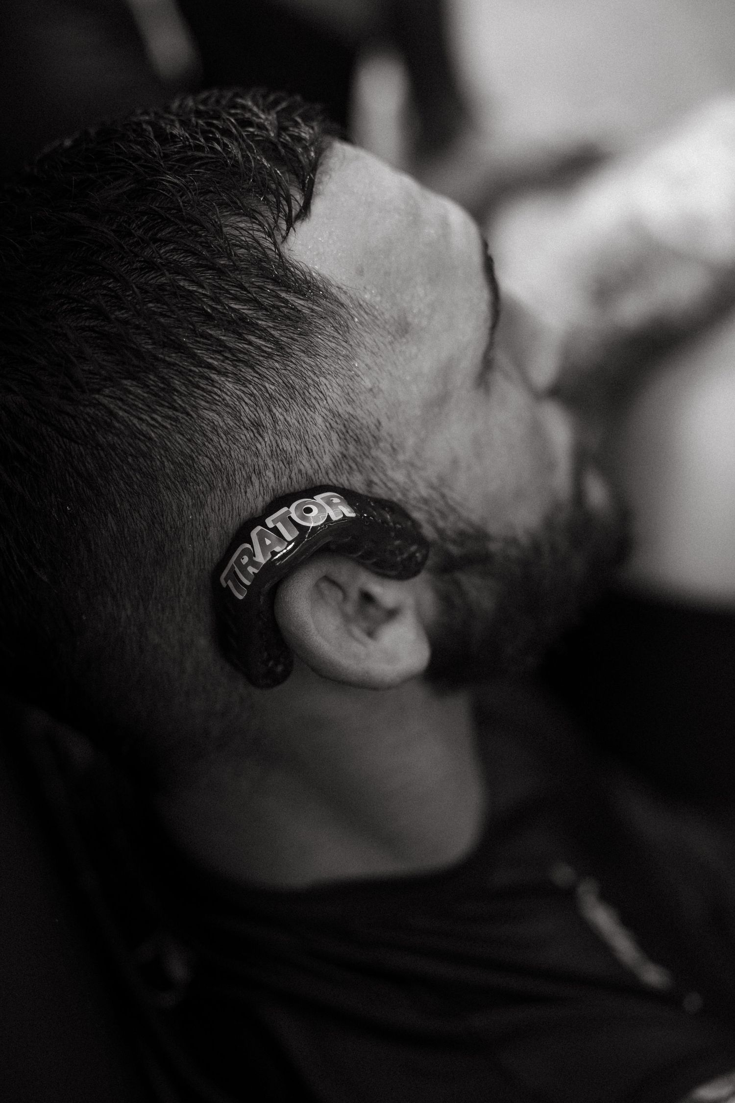 Black and white close-up of a man with a Traitor logo shaved into his hair above the ear.