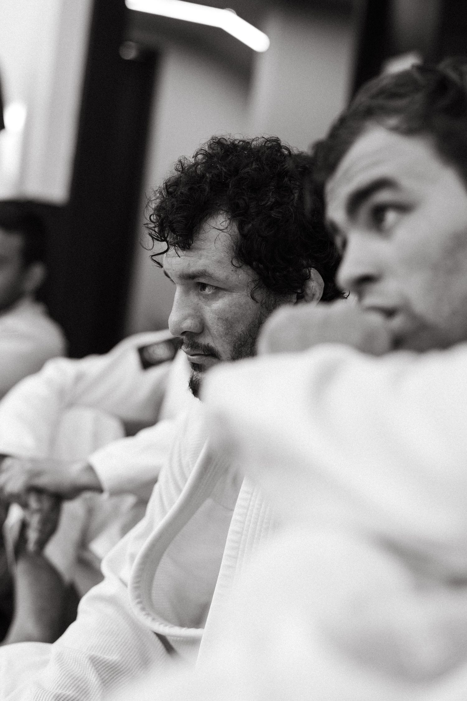 Black and white photo of two men in white martial arts gi uniforms sitting together at a judo or jiu-jitsu event.