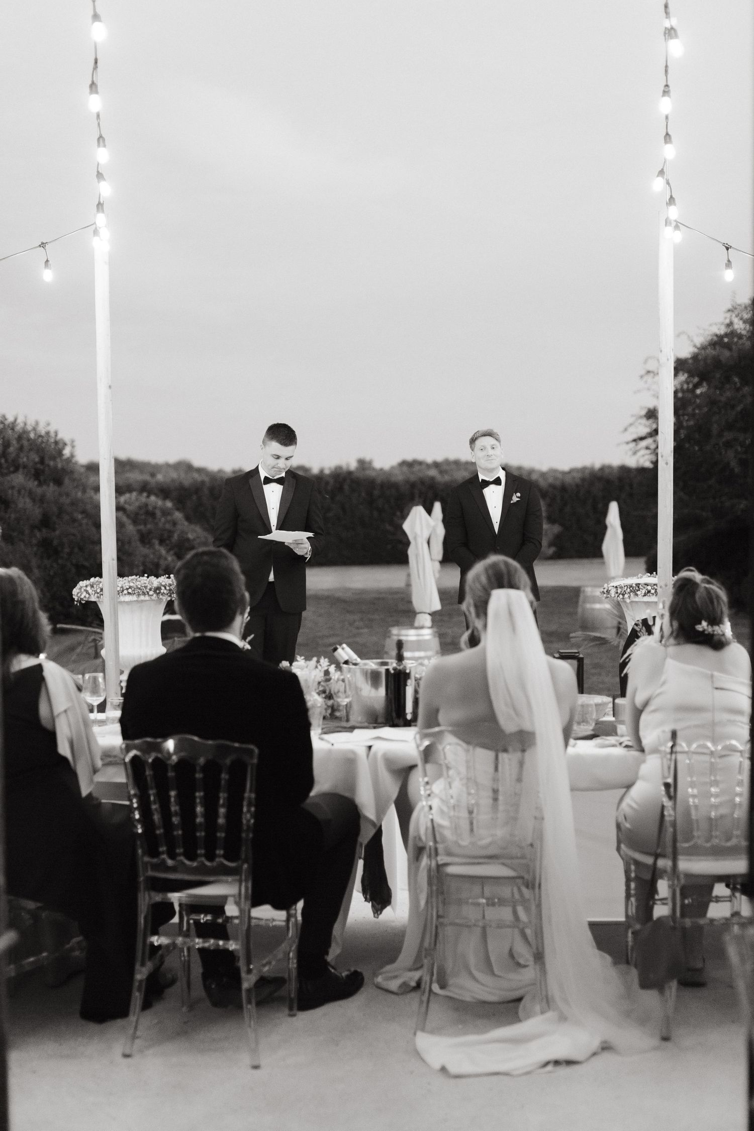 Black and white panoramic photograph showing an elegant outdoor wedding reception with tables and chairs set up on a patio.