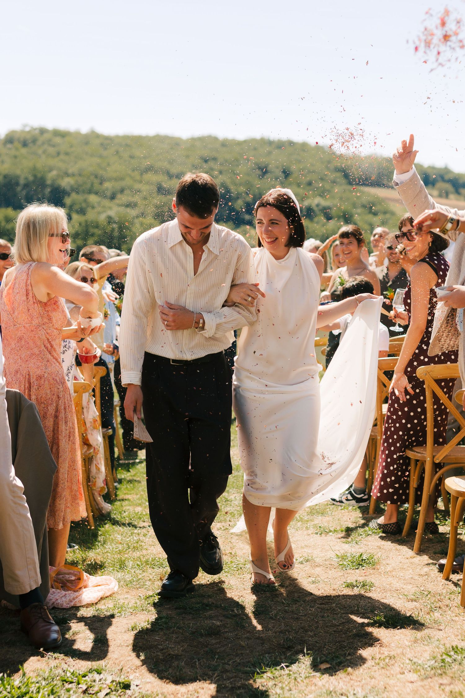 Wedding guests celebrate with joyful dancing in an outdoor summer ceremony under bright sunlight.