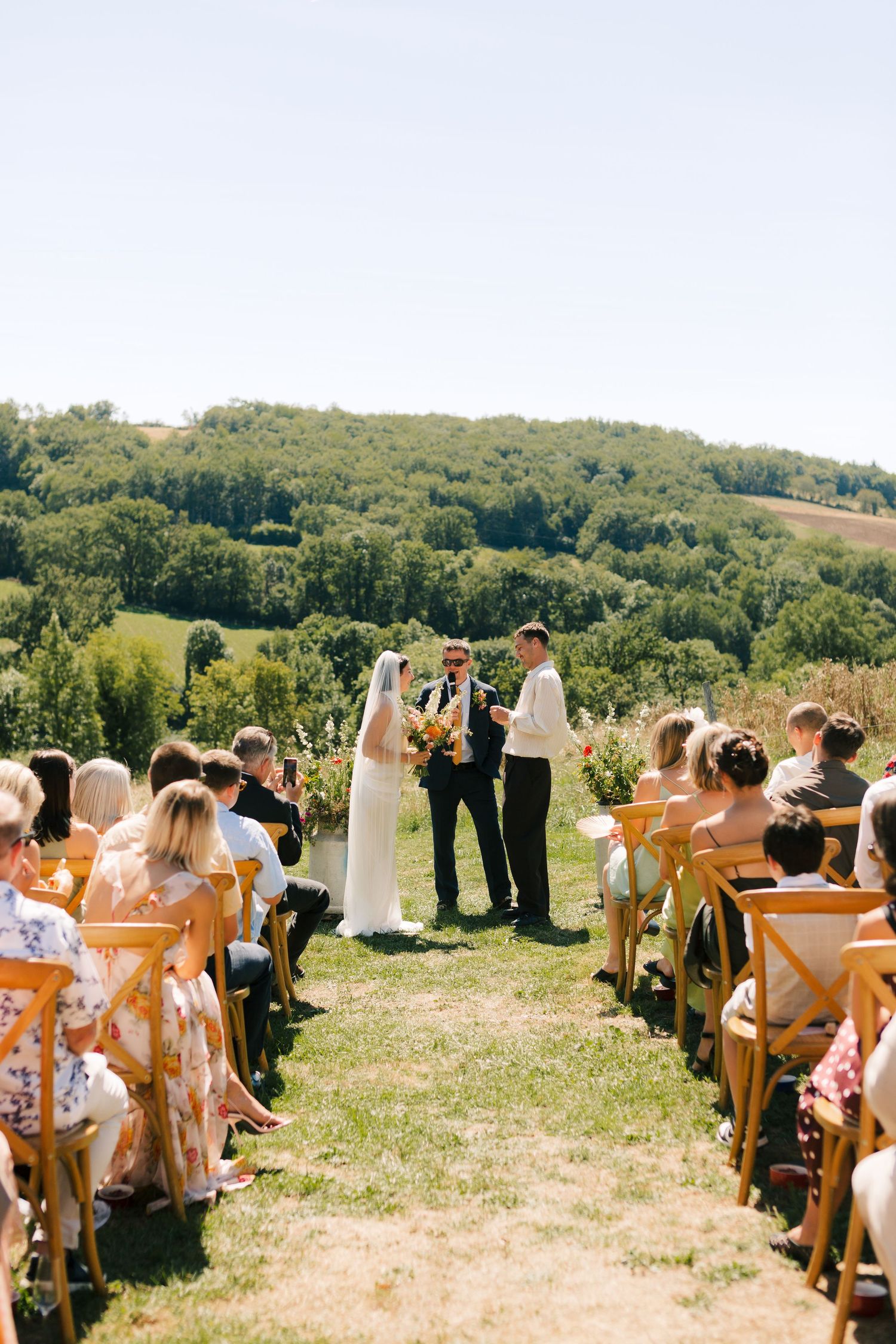 Outdoor wedding ceremony setup with wooden chairs on a grassy hilltop overlooking scenic countryside views.