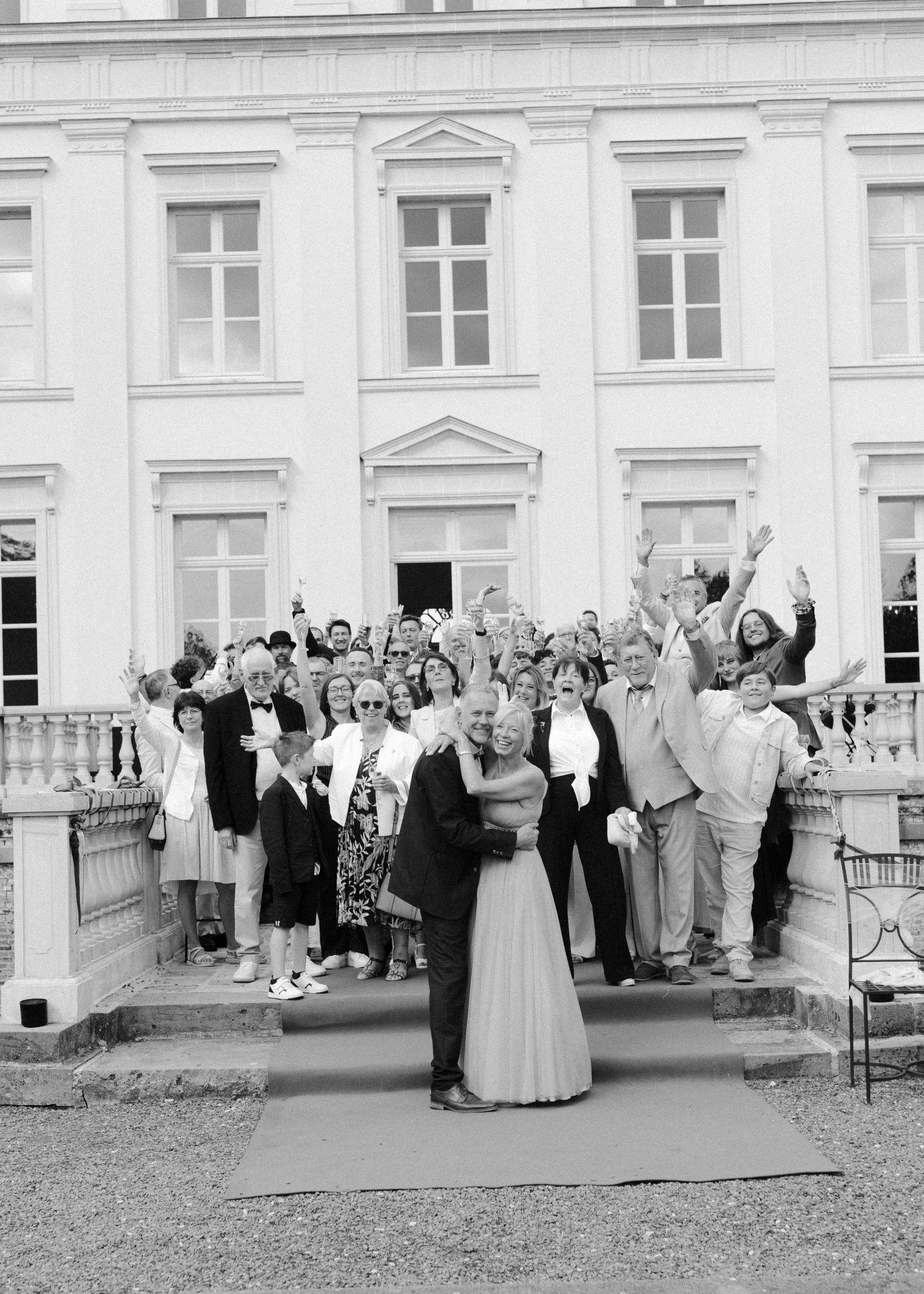 A black and white panoramic photograph shows wedding guests gathered outside a grand historic building.