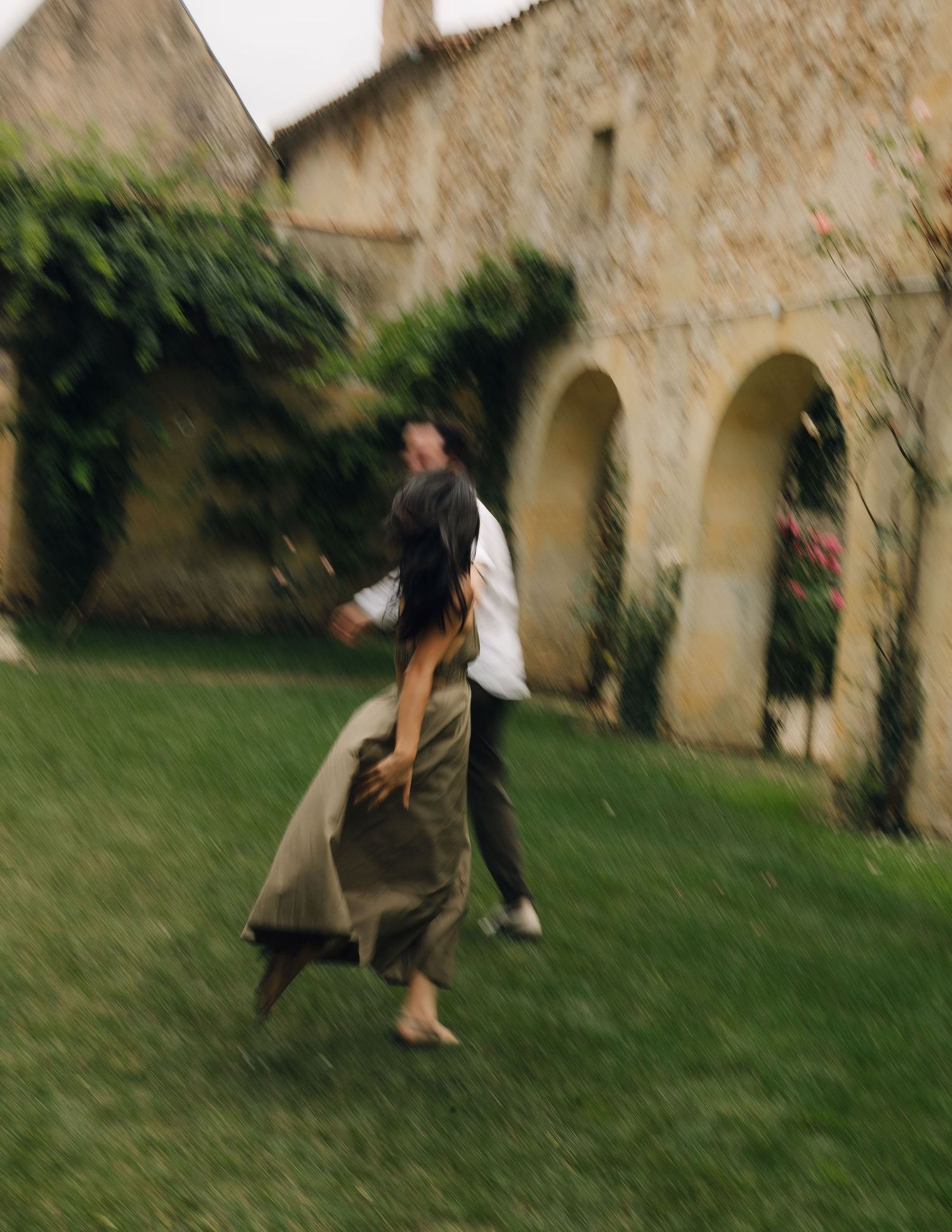 A sequence of motion-blurred photos showing someone jumping and falling on a grassy lawn beside a stone building.
