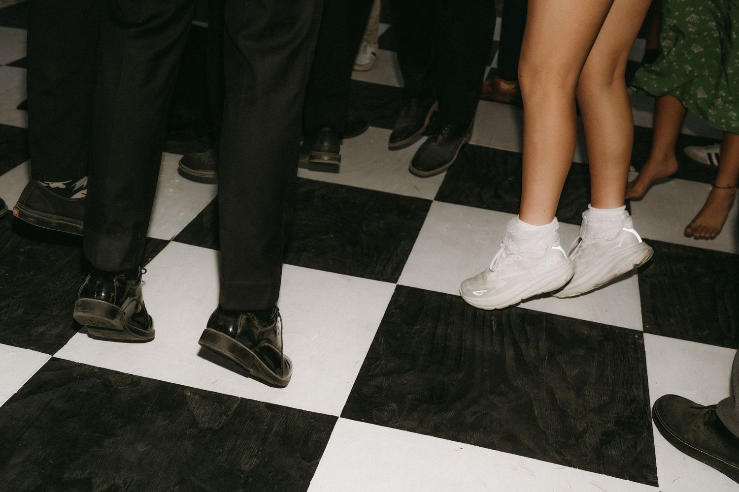 A row of people's feet and legs standing on a black and white checkered floor.