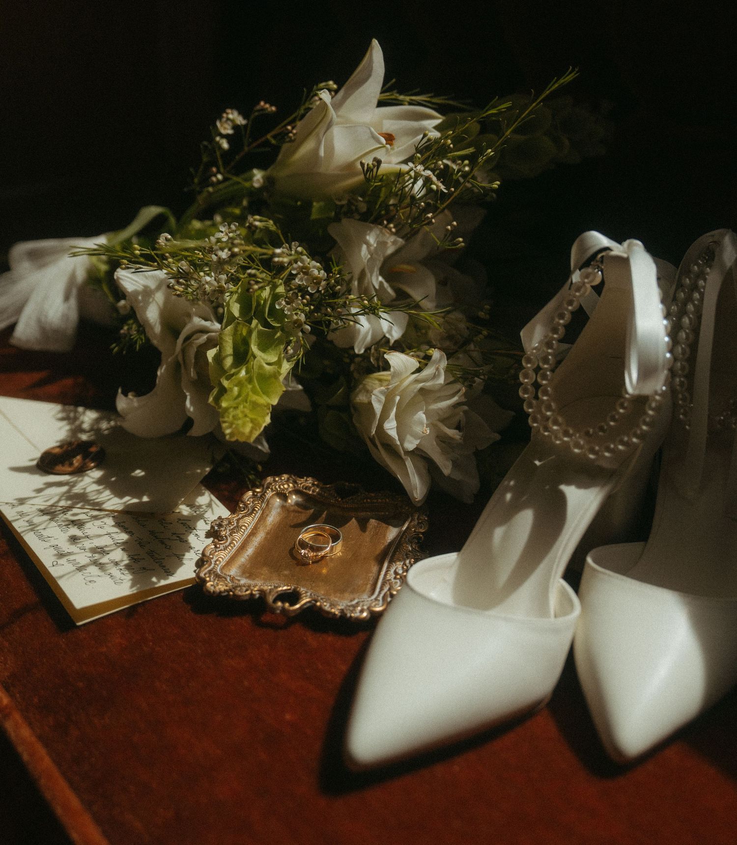 White bridal heels surrounded by delicate floral arrangements on a dark wooden surface.