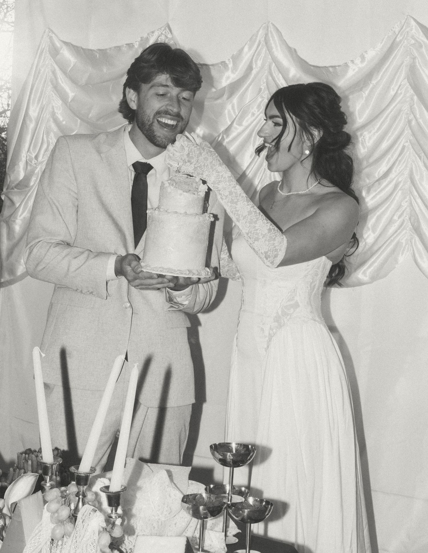 Black and white photo series showing a couple in wedding attire cutting cake and feeding each other during a reception.