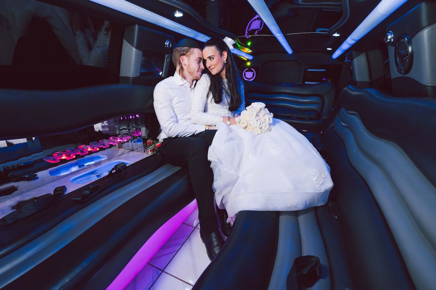 Bride and groom sitting together inside a luxurious stretch limousine with purple LED lighting on their wedding day.