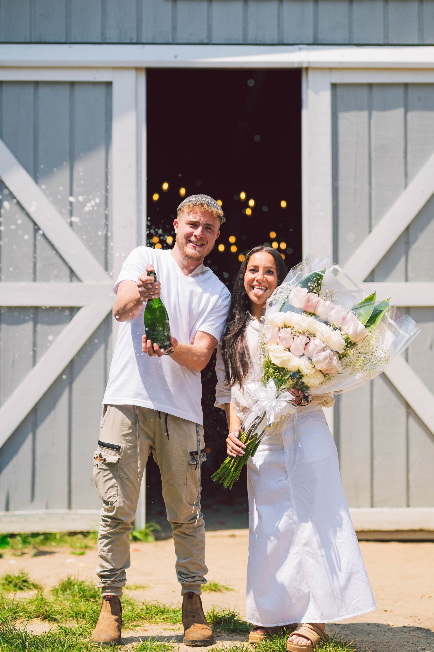 Playful engagement photos outside a rustic barn with champagne pop and laughter.