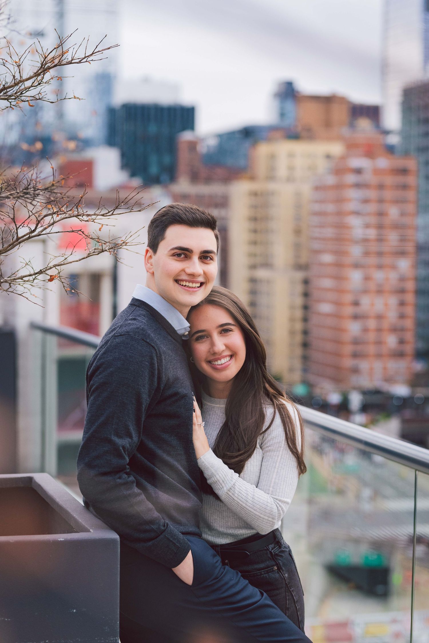Couple embracing on rooftop terrace with Manhattan skyline in background.