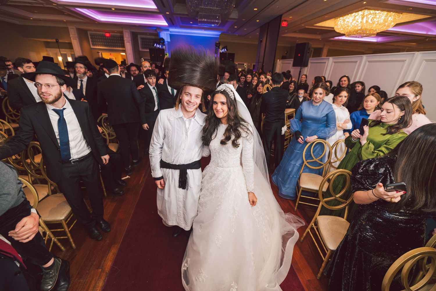 Elegant wedding reception venue with purple lighting and guests mingling at decorated tables.