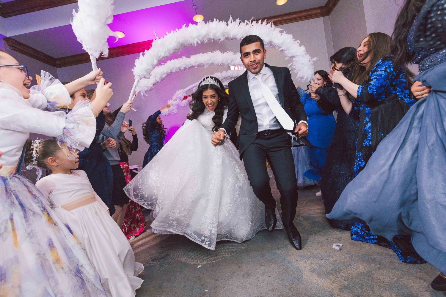 Wedding celebration with flowing white dress amid purple lighting and dancing guests.