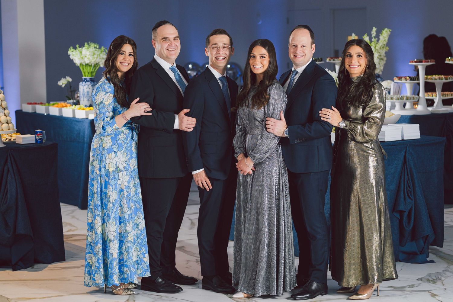 Group photo of formally dressed guests at an elegant indoor event with blue lighting.
