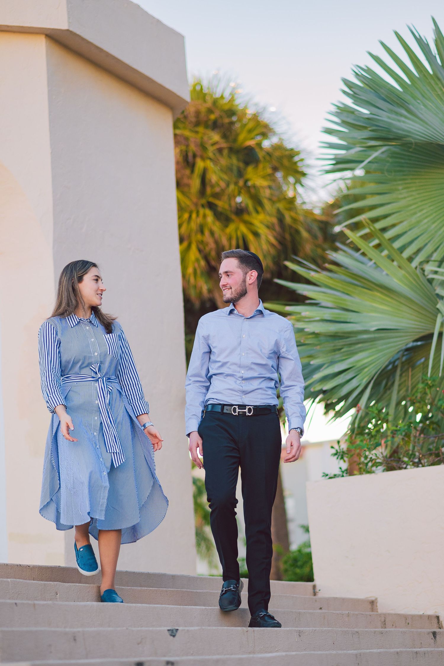 Couple walking down outdoor steps with palm trees in the background.