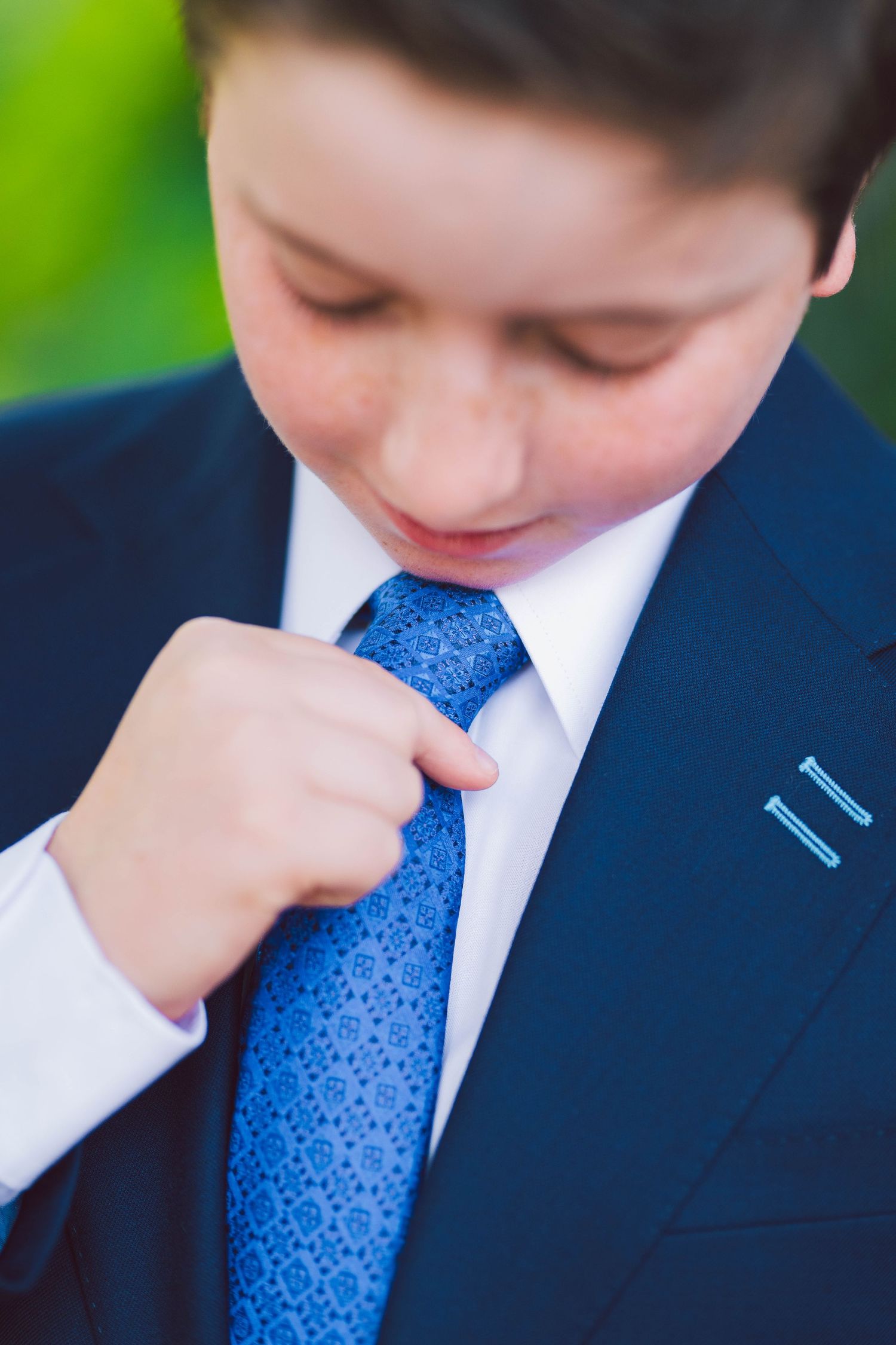 Close-up of adjusting a bright blue patterned tie with a navy suit and white shirt.
