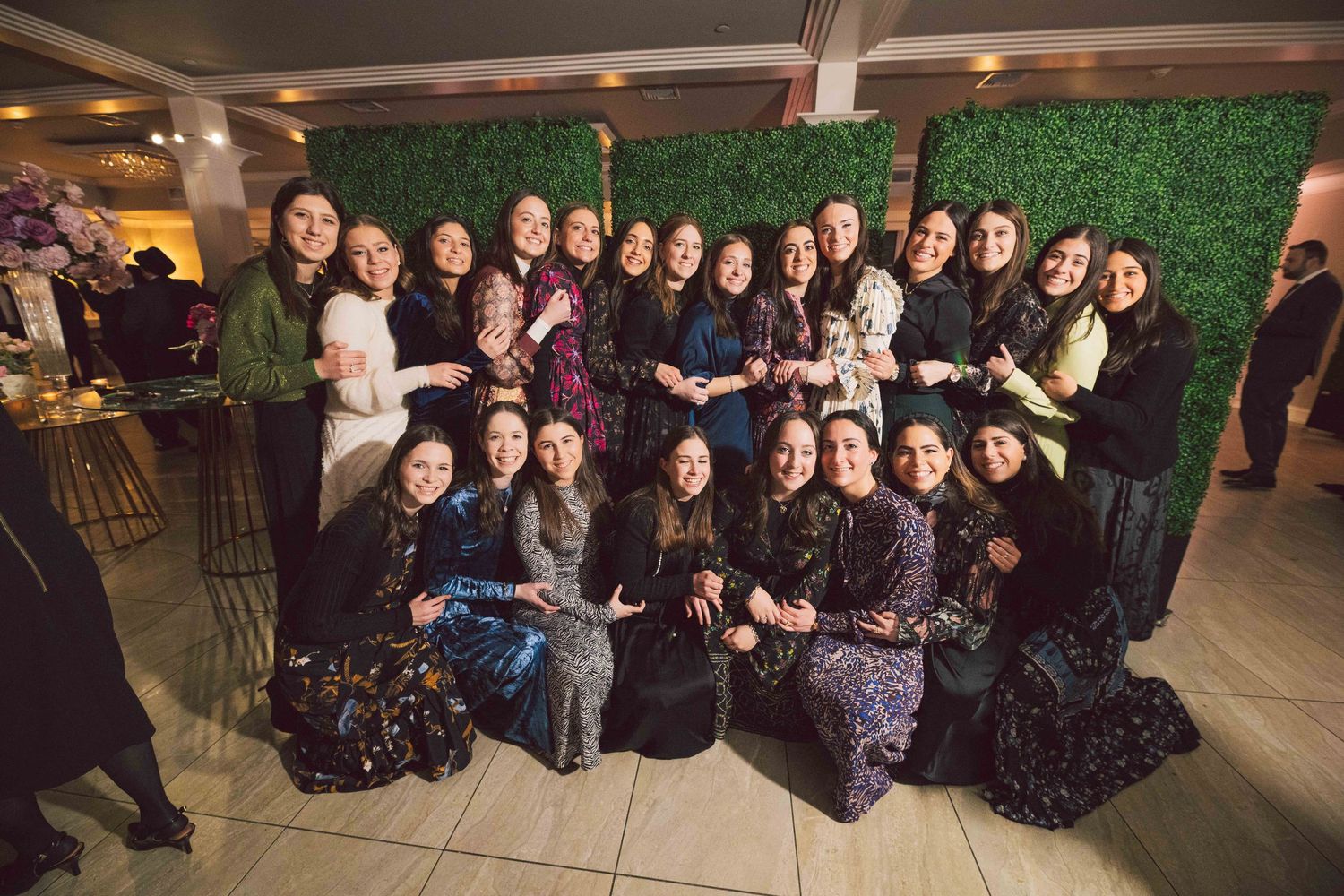 Large group photo of people posing together against a green wall backdrop at an indoor event.