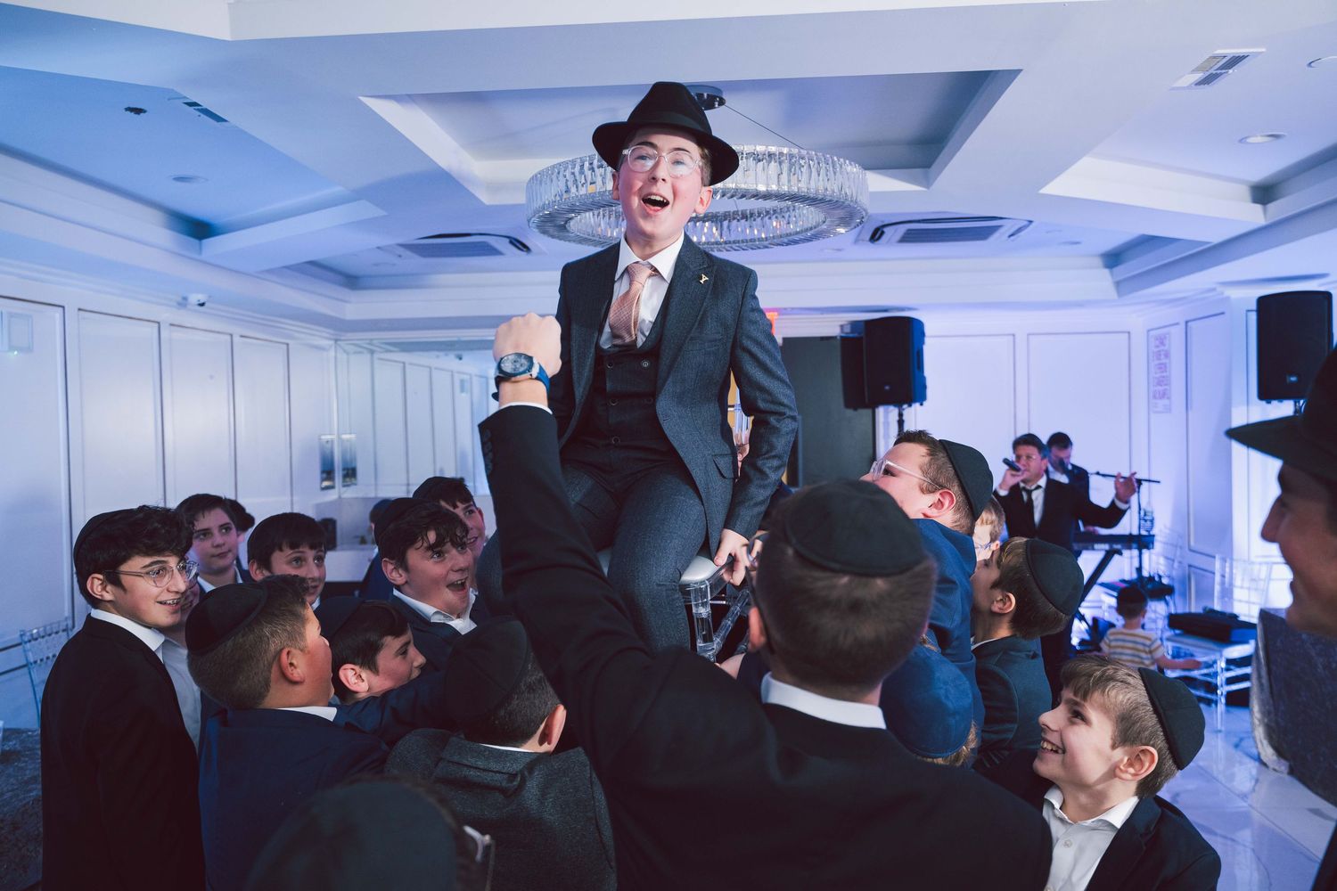 A celebration at a Jewish wedding reception shows guests lifting someone on a chair during the traditional Hora dance.