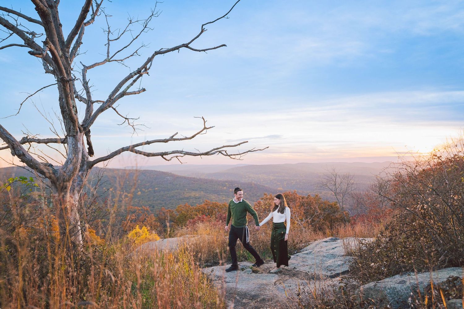 People enjoy a scenic mountain overlook during autumn as golden light illuminates the rolling landscape below.