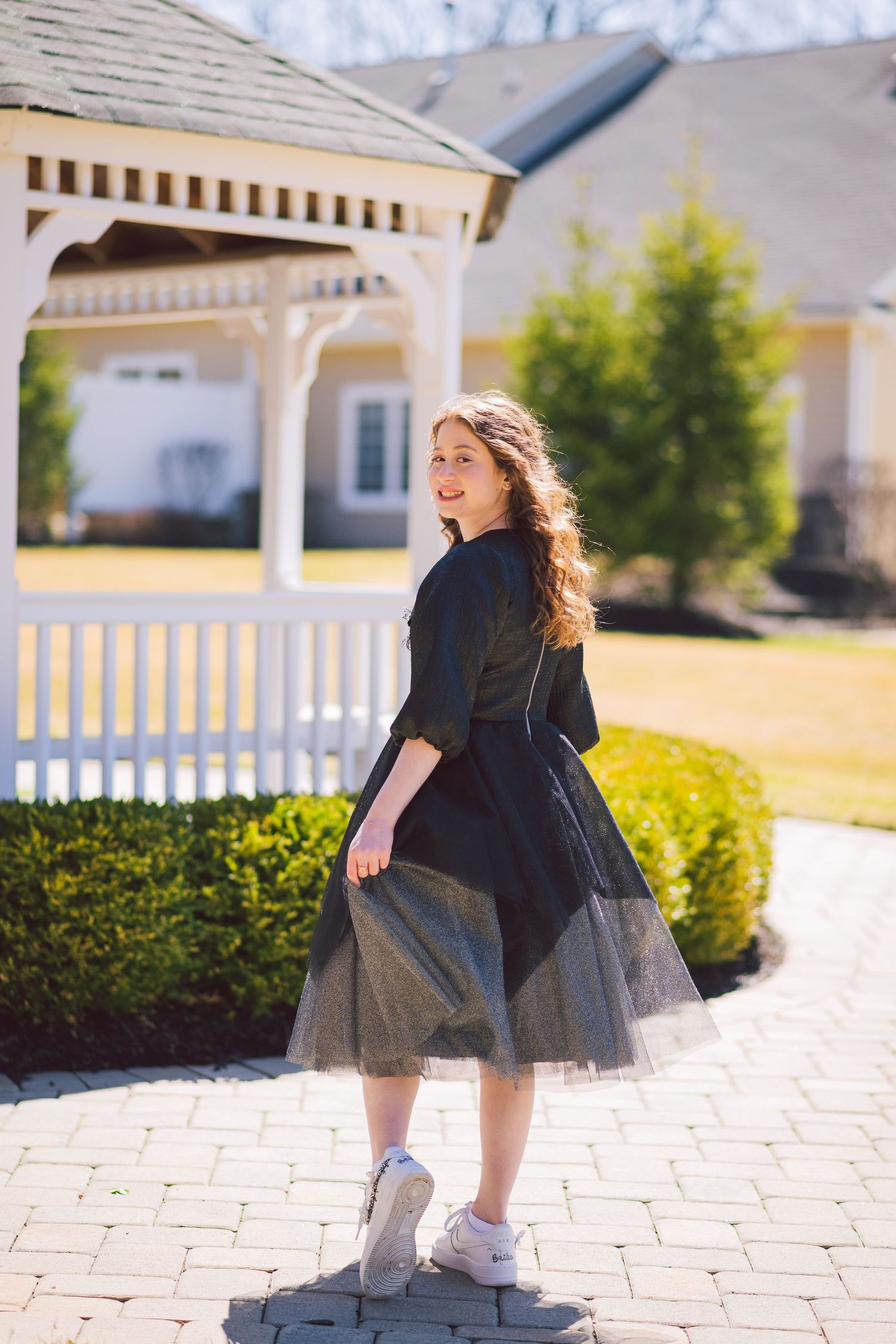Person in a black tulle dress twirling on stone pavers near a gazebo.