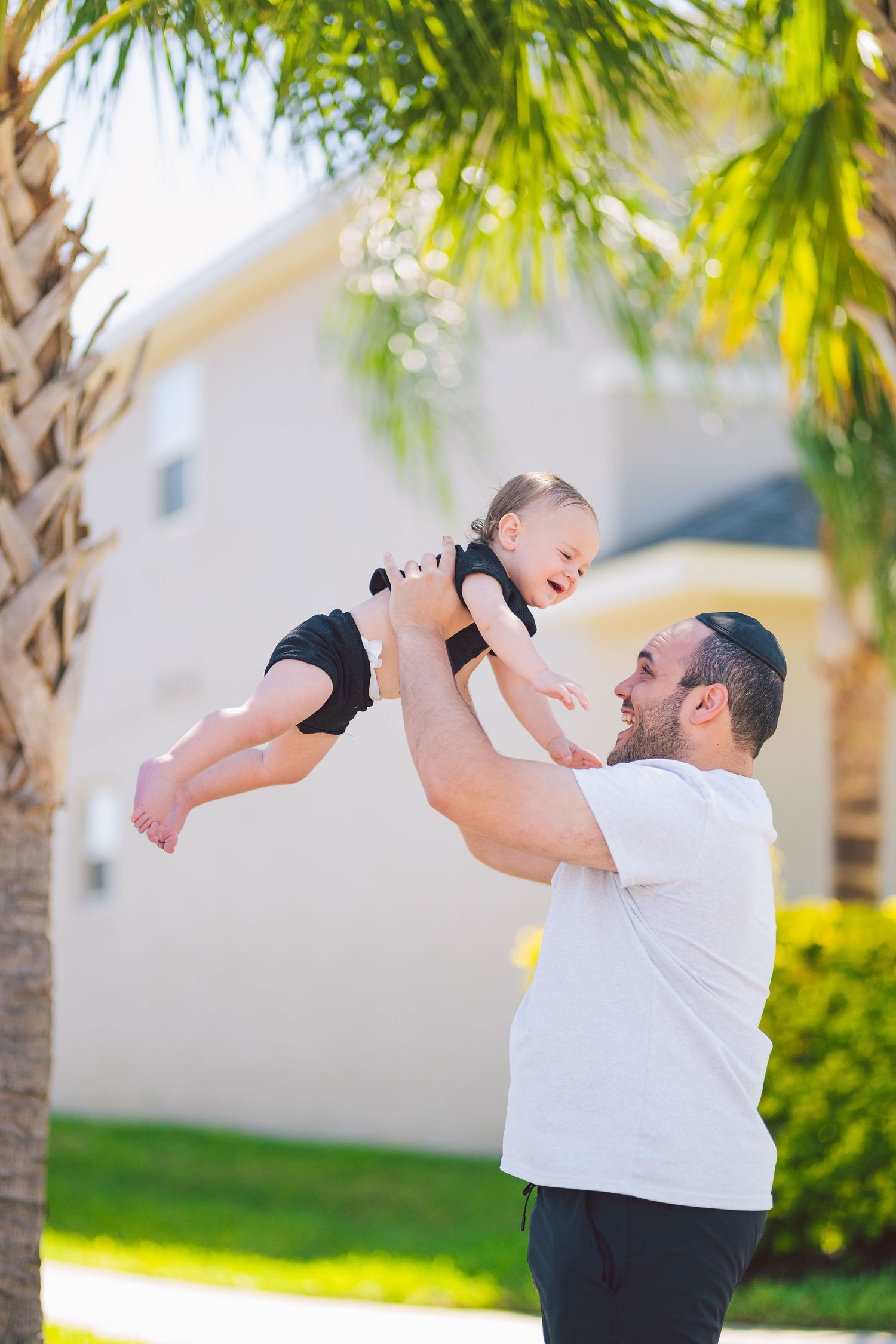 Playful outdoor portrait showing joyful interaction under palm trees on a sunny day.