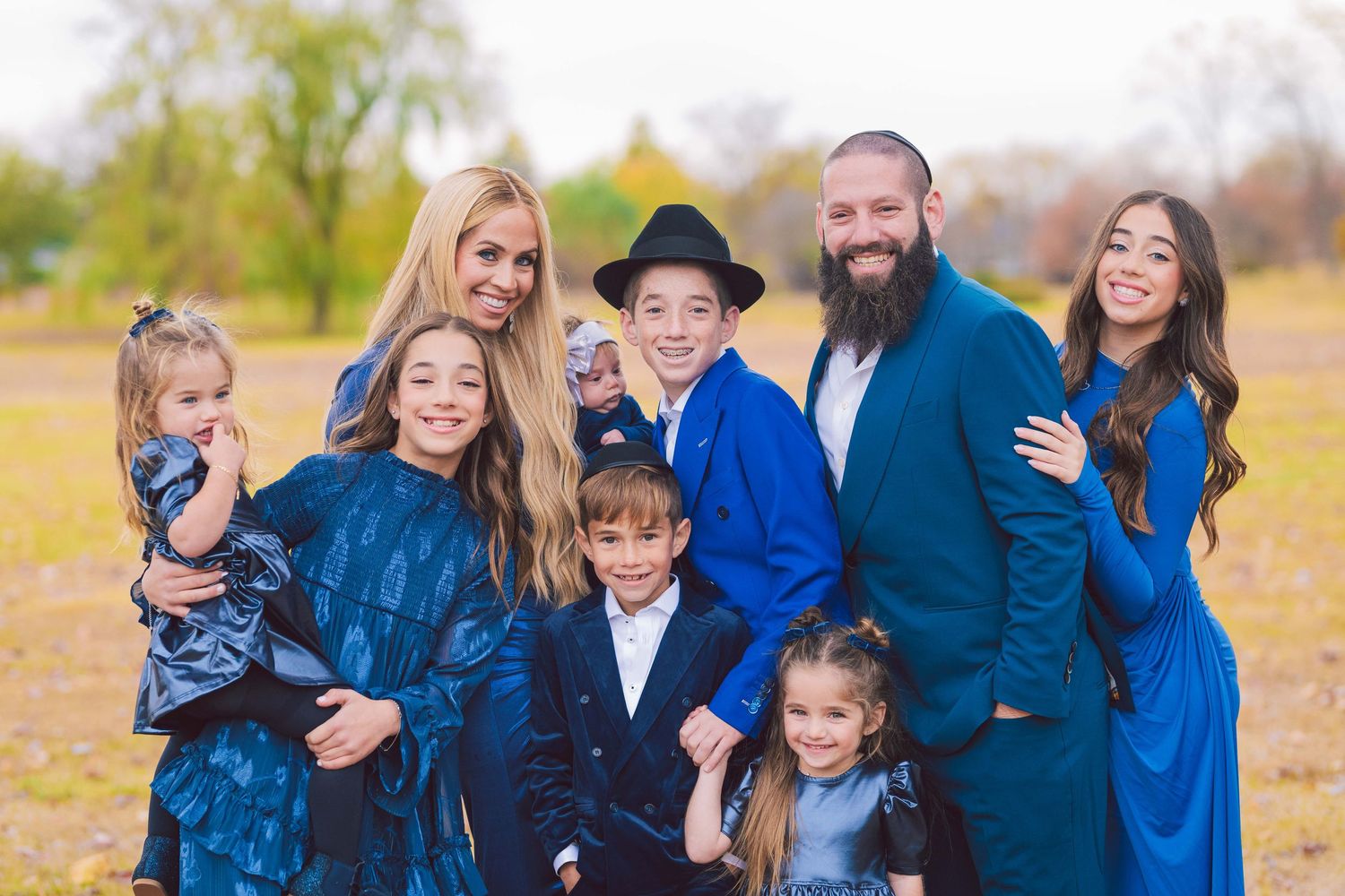 Large family group wearing coordinated blue outfits poses together outdoors in casual setting.