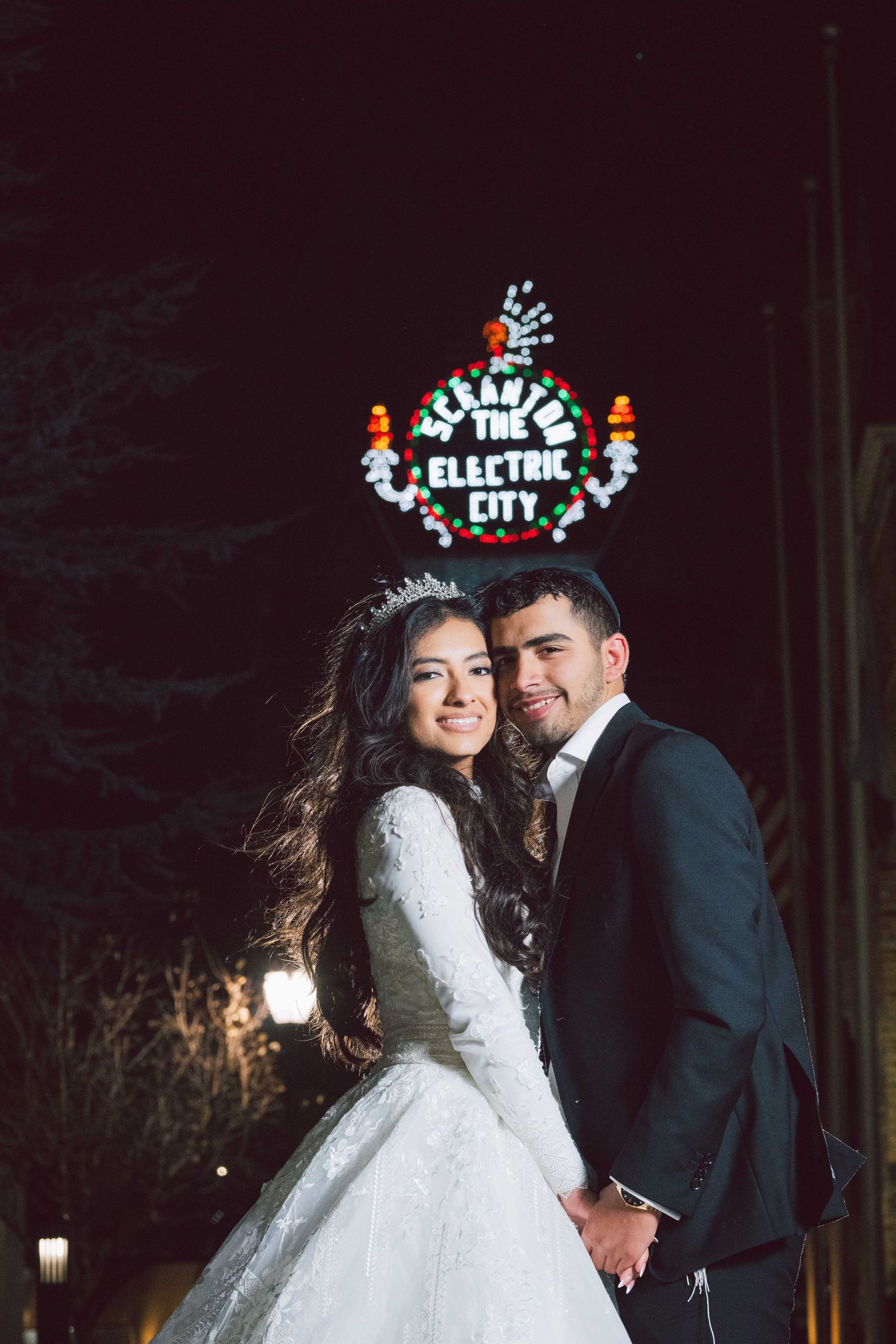 Wedding couple poses under illuminated electric city sign at night.