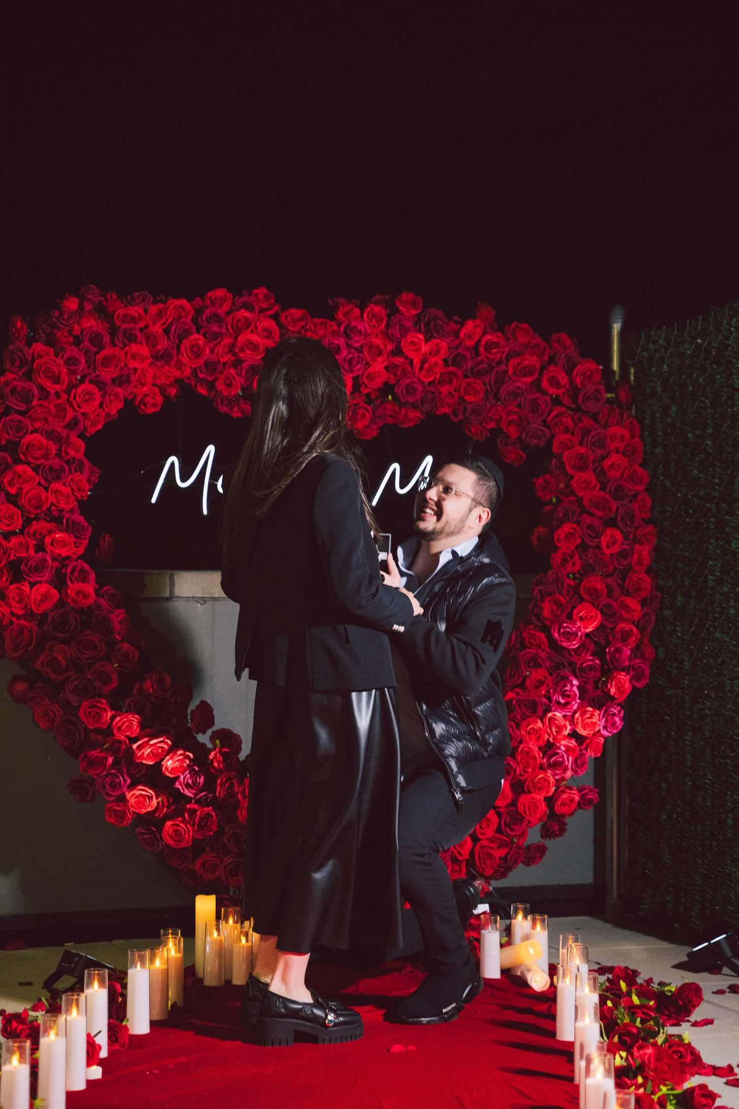 Romantic proposal setup with red rose heart backdrop and glowing candles creating an intimate atmosphere.