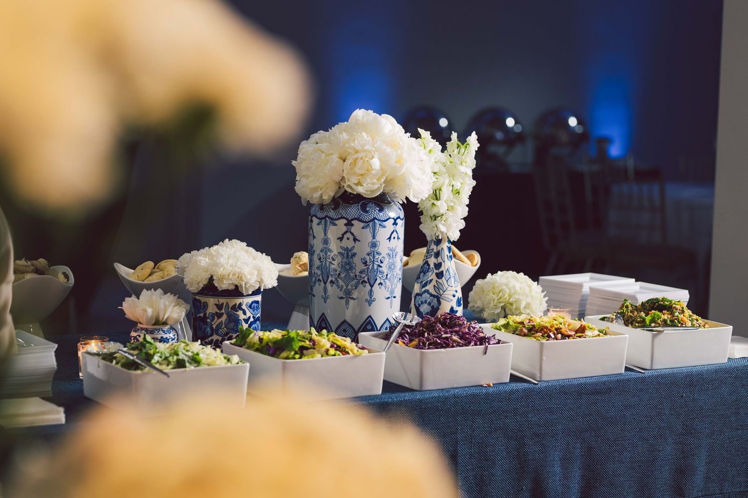 Elegant wedding reception decor with white floral arrangements and blue mood lighting.