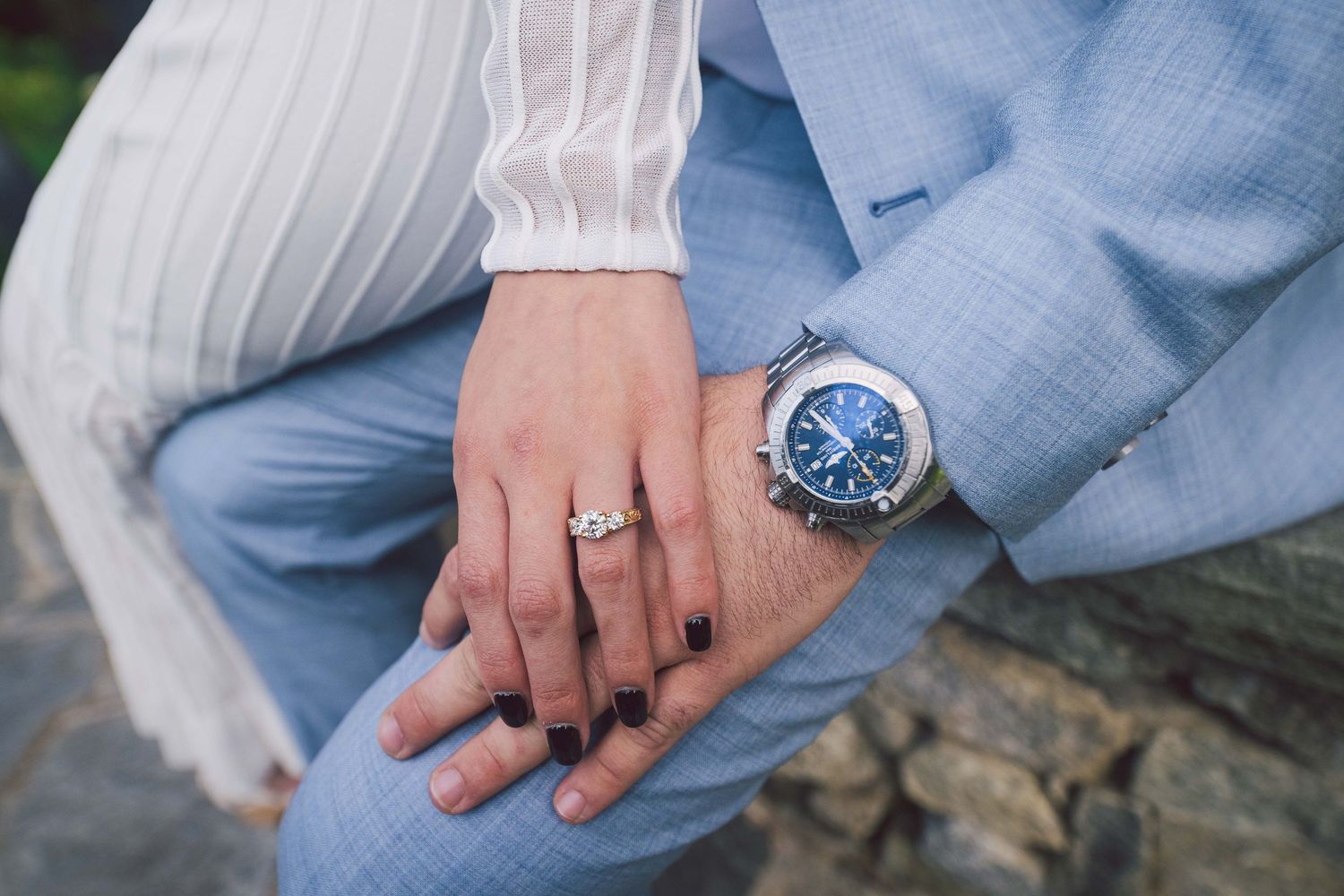 Close up detail shot of hands with wedding rings against light blue suit fabric.