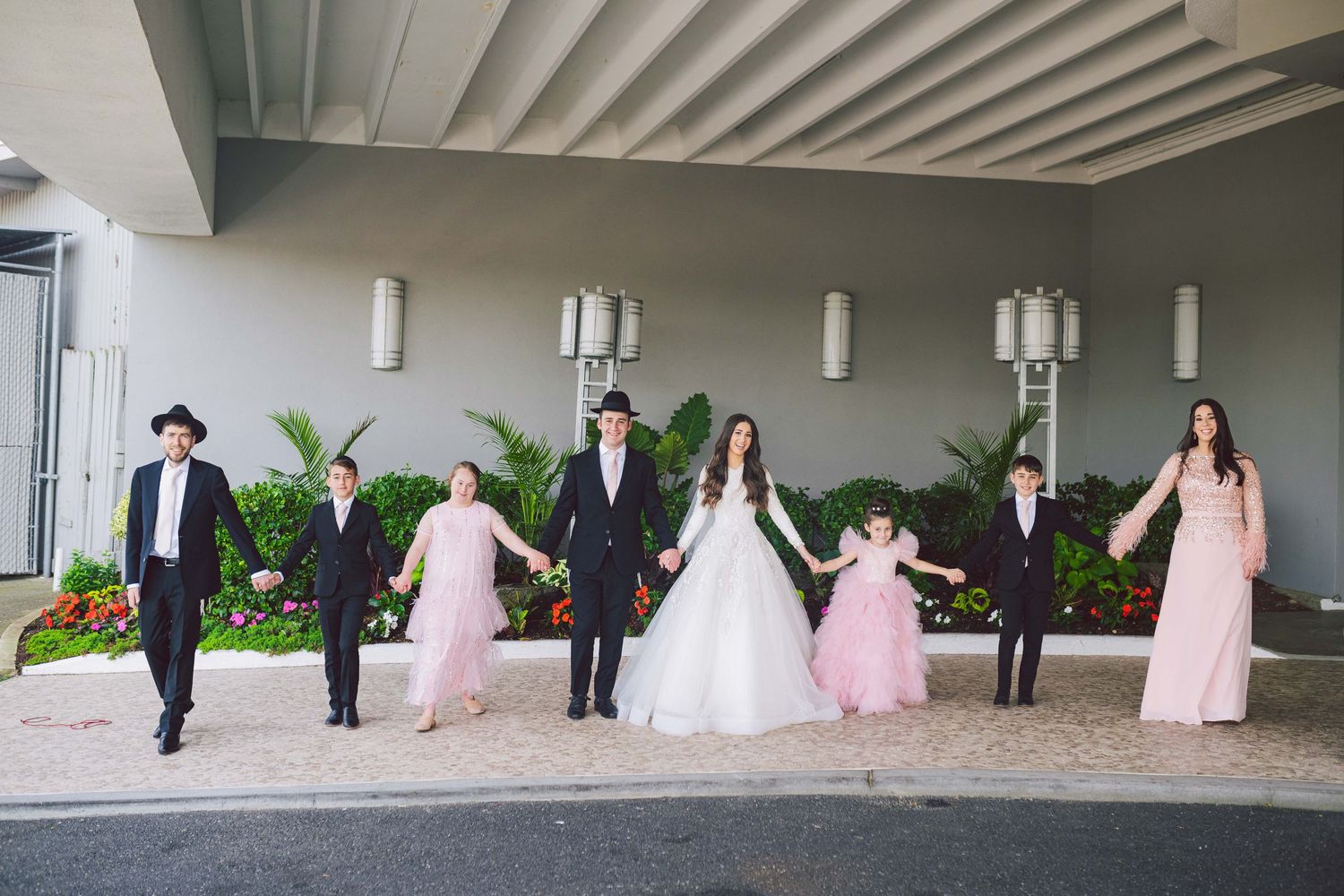 A wedding party lined up along a modern architectural walkway with columns.